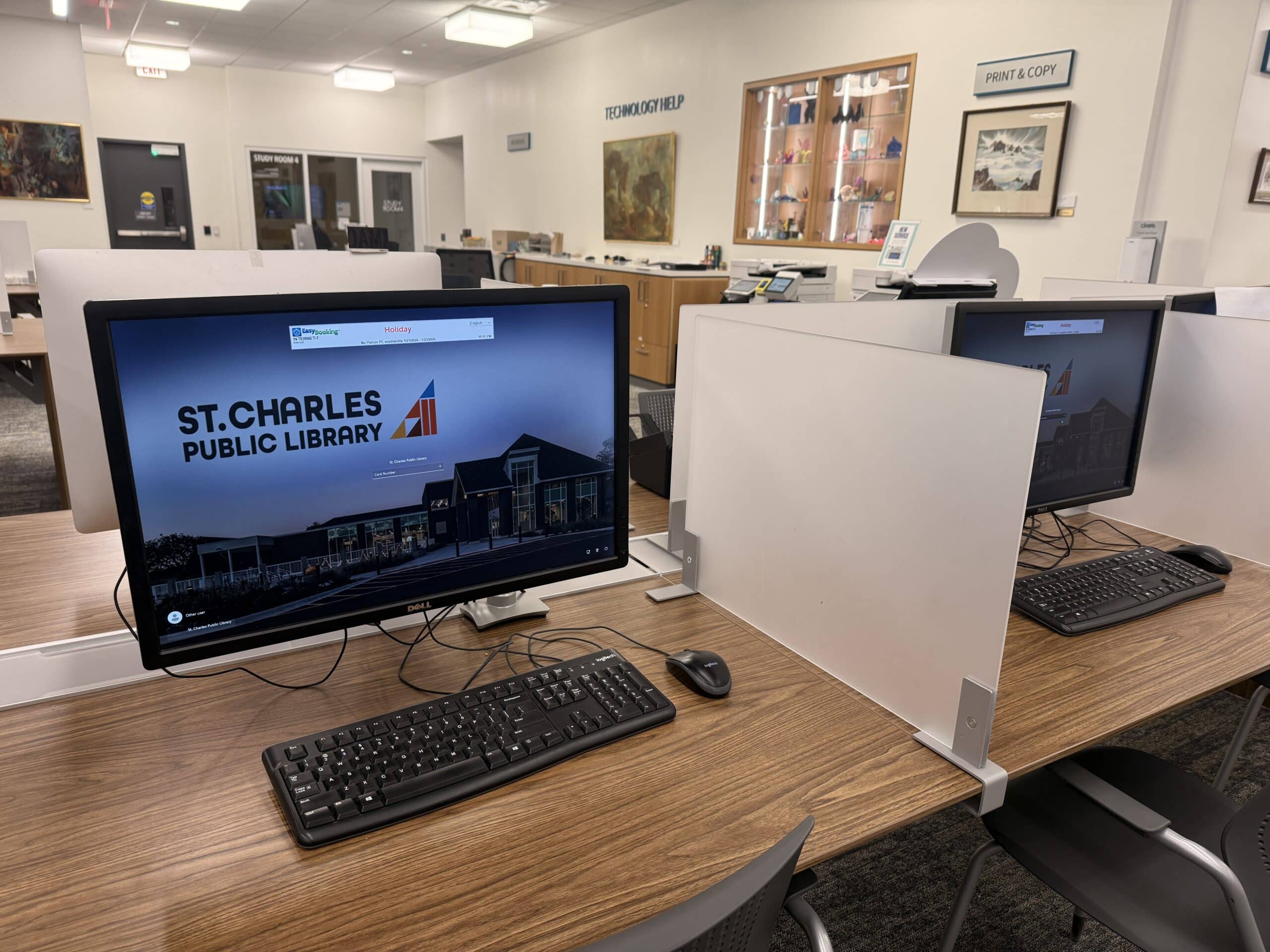 Computer screen, keyboard, mouse on a desk in a library.